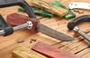 Custom knife blade clamped with a wooden handle blank and colorful stabilized wood pieces on a workbench.
