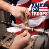 Hands sanding a wooden spindle on a lathe with an American flag backdrop and Turn for Troops logo