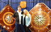 Two people standing in front of large wooden compass rose marquetry panels with intricate inlay and nautical designs