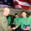 Military personnel in green shirts exchanging handcrafted wooden pens in workshop setting with American flag backdrop