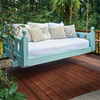 Suspended painted wooden outdoor daybed with decorative pillows on wooden deck surrounded by greenery