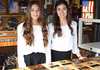 Two young women standing behind a woodworking display table with plaques in a workshop setting
