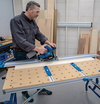 Man using a track saw on a workbench with clamped guide rails in a woodworking shop