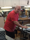Man in red shirt using a jointer to smooth a wooden board in a workshop.