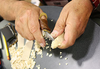 Hands carving a small wood piece with a folding pocketknife, surrounded by wood shavings