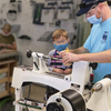 Adult and child wearing masks turning a wooden pen blank on a lathe in a workshop