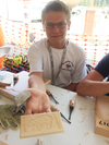 Young woodworker showing a carved wooden panel with a bear design using carving gouges on a workshop table