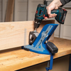 Hand using cordless drill with pocket hole jig clamped to wooden workbench drilling angled pocket holes in wood panel