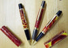 Three custom acrylic pens with red, yellow, and black swirled barrels and matching caps on a wooden surface