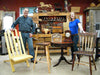 Two woodworkers standing beside handmade wooden chairs and furniture in a workshop filled with woodworking tools and