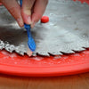 Hand scrubbing resin and debris off a circular saw blade with a toothbrush on a red tray