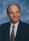 Headshot of a man in a suit and patterned tie against a blue studio backdrop