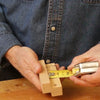 Hands using a tape measure and wooden gauge block to mark precise length on hardwood piece