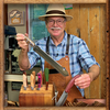 Woodworker in apron and hat holding a Japanese pull saw in a workshop with various hand tools on a wooden block.