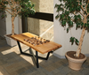 Live-edge wooden bench with metal legs holding a wooden chessboard, flanked by potted trees indoors.