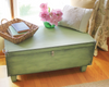 Green painted wooden storage chest with simple latch, holding a basket and flower vase on top near window