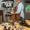 Woodworker using drill press with various sanding and grinding accessories on workbench nearby