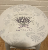 Round wooden stool painted white with a transferred image of lavender sprigs and vintage script on the seat surface
