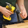 Person holding a cordless drill with a magnetic tip picking up a screw over a wooden workbench.
