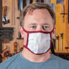 Man wearing a cloth dust mask in a woodworking workshop with hand tools on the wall behind him