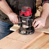 Hands adjusting a Skil router on a wooden board to create a straight groove.